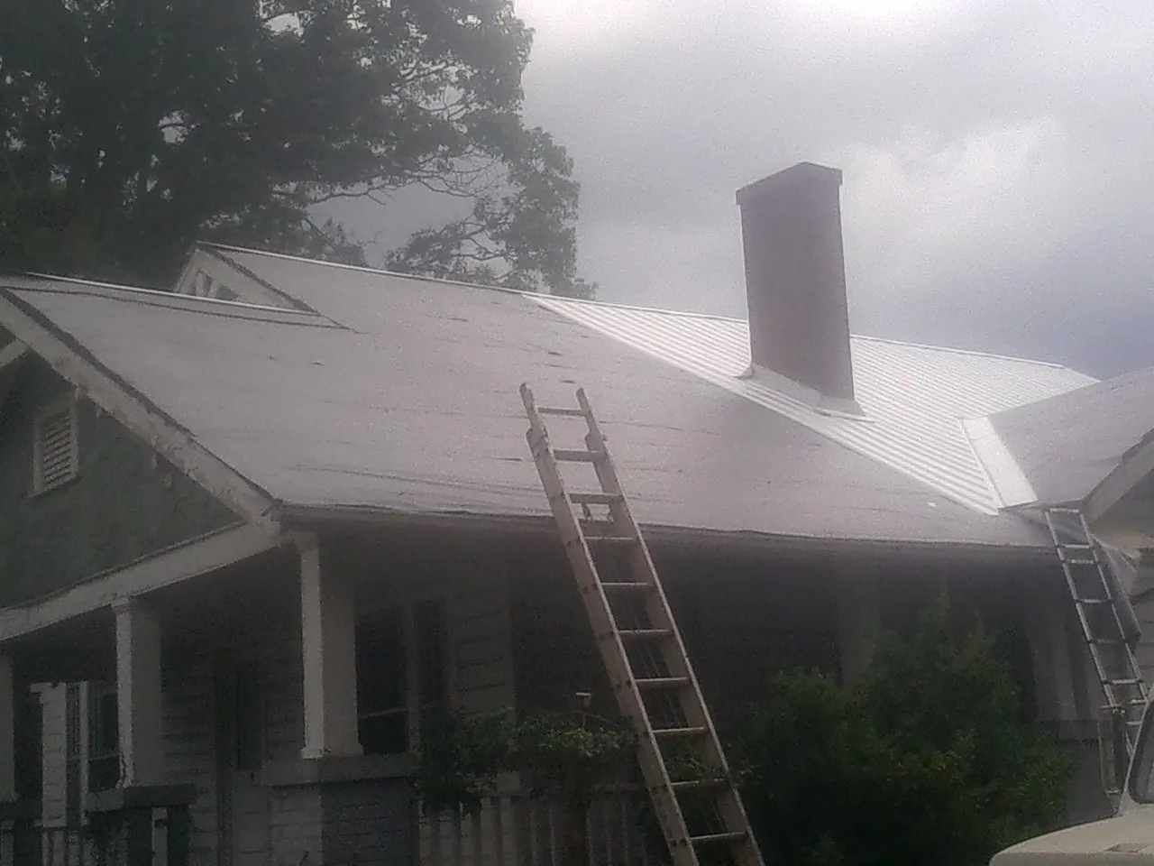 Ladders against a metal roof on an older home with a brick chimney in Ewing