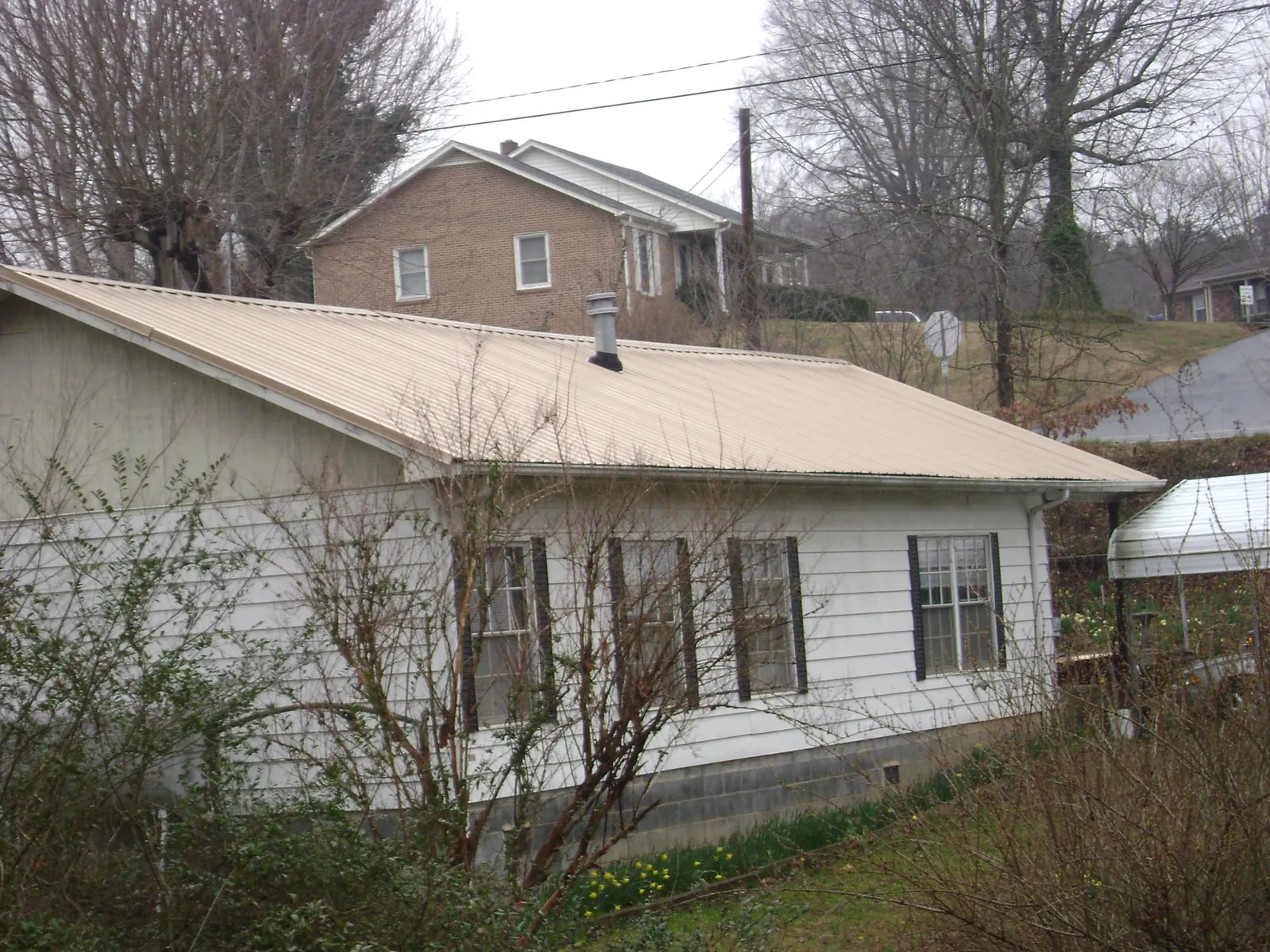 Tan metal roof on a white sided house set into a hillside — Commercial Roofing by Roofing Brothers in Ewing